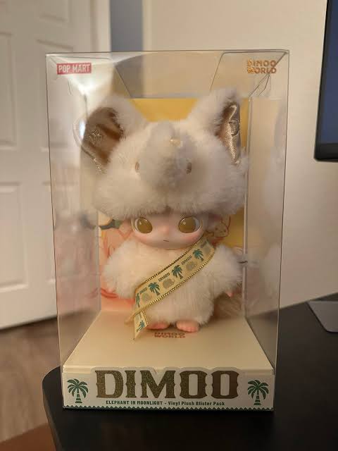 Plush toy in a clear packaging with 'DIMOO' branding on a wooden surface.