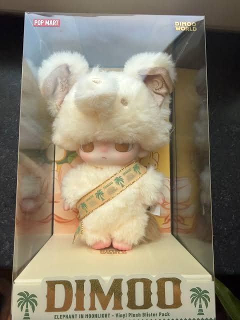 Plush toy with a sash in a clear packaging box, featuring the brand 'DIMOO'.